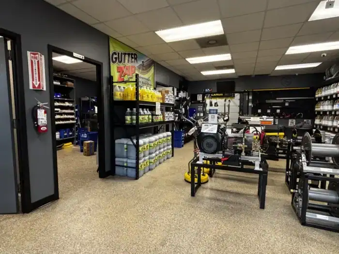 A commercial supply room with shelves of cleaning products, large containers, equipment, and a "Gutter Zap" banner on the wall.