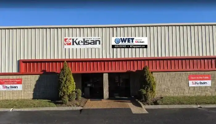 Front exterior of a commercial building with "Kelsan" and "WET" signage above the entrance, two trimmed trees, and signs indicating the location is open to the public.