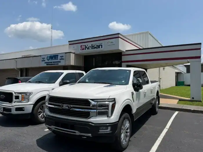 Two white Ford pickup trucks parked in front of a commercial building with a sign that reads "Kelsan" above the entrance.