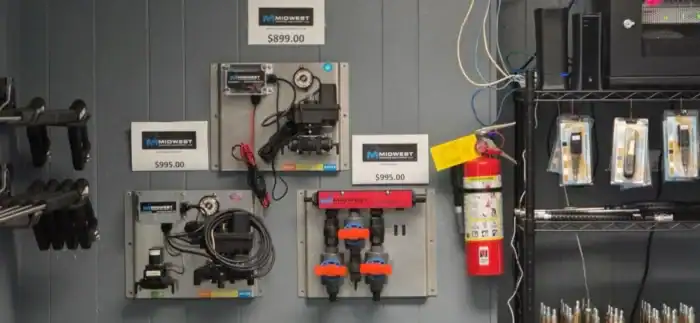 Control panels and electronic equipment are mounted on a gray wall with visible cables, price tags, and a red fire extinguisher hanging nearby.